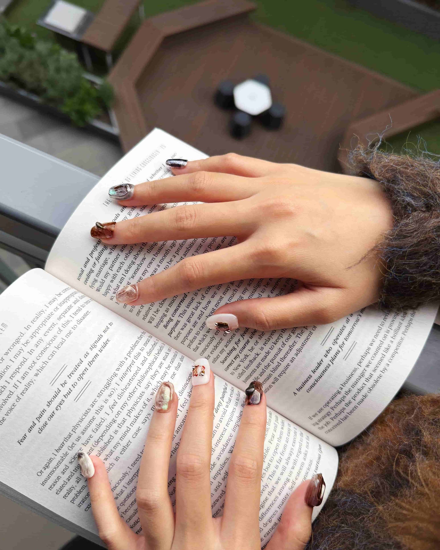 Luxury press-on nails in earthy marble tones styled while reading a book, Ethereal Terrain set by Nailrative.