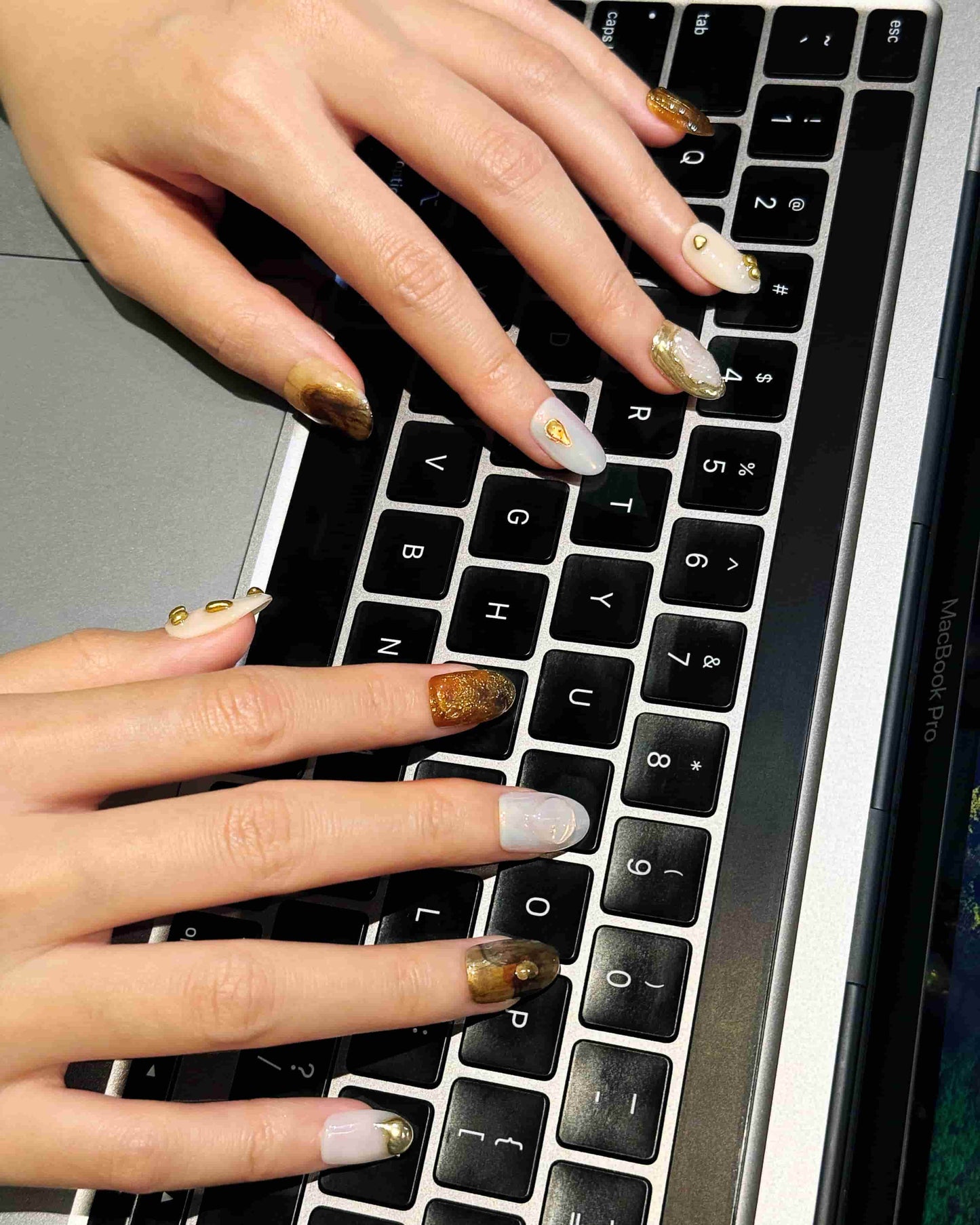 Gilded Mirage luxury press-on nails by Nailrative with metallic gold and neutral tones, styled in a modern workday typing scene.