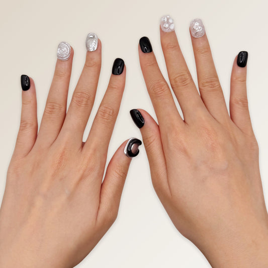 Two hands with black and silver nail polish on a plain background