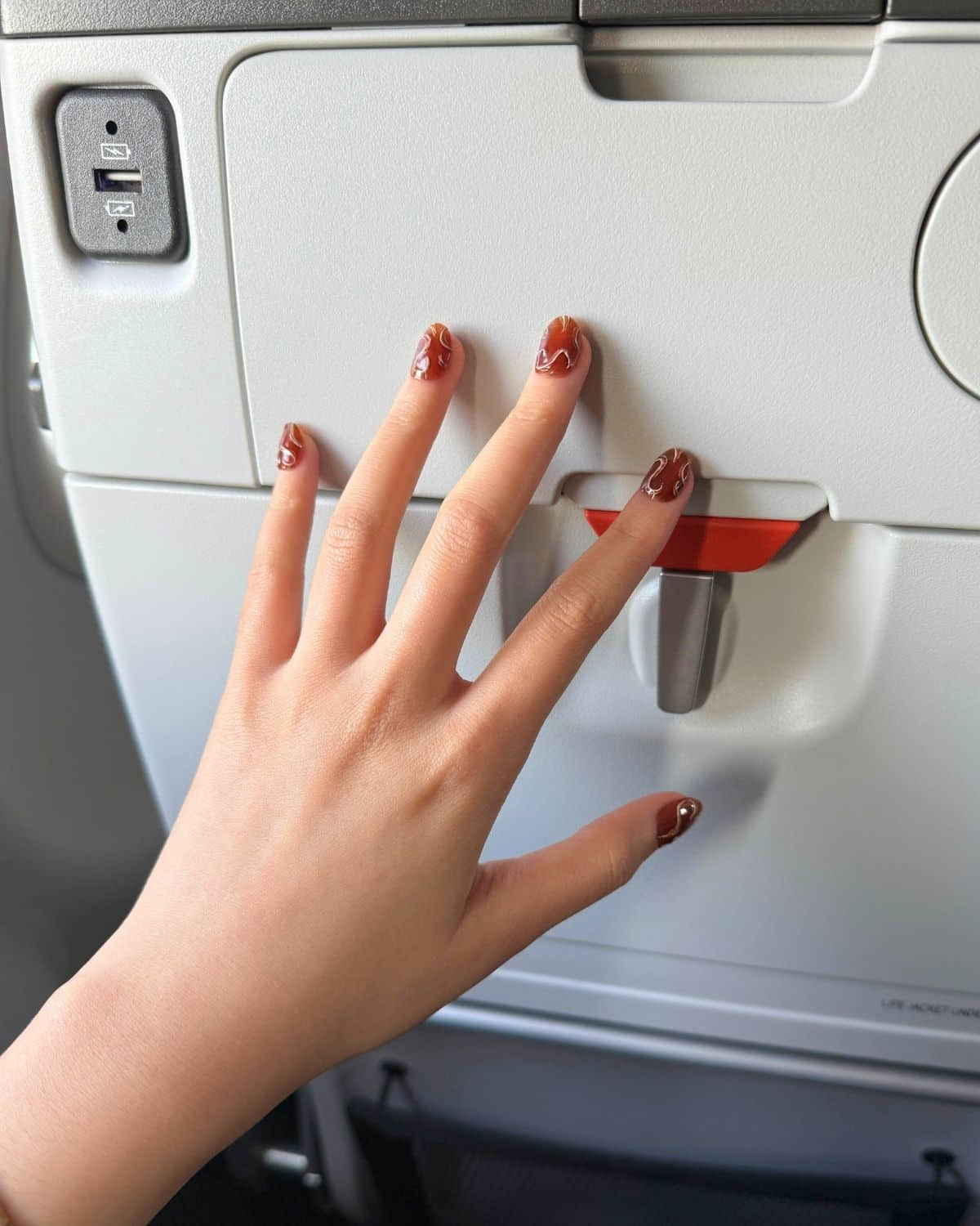 Mocha Trace luxury press-on nails by Nailrative with marble swirl design, photographed on an airplane tray table for a chic travel-inspired manicure.
