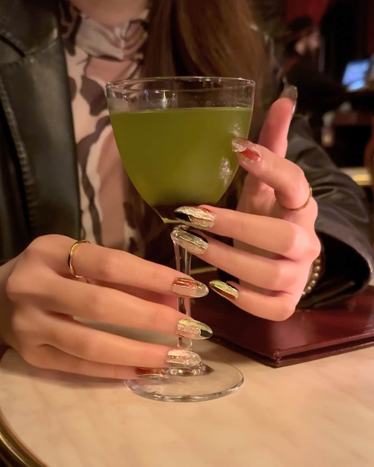 Press-on nails with bold design holding cocktail glass in low-lit bar.