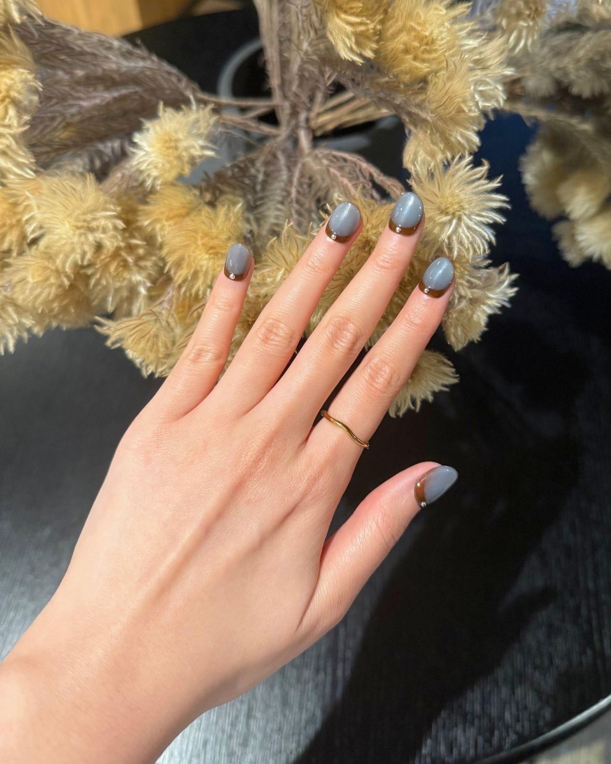 Sienna Mist press-on nails by Nailrative, glossy ombré in slate blue and sienna brown with metallic stud detail, styled with yellow flowers. Handmade, reusable nails from the Éclectique Harmony collection.