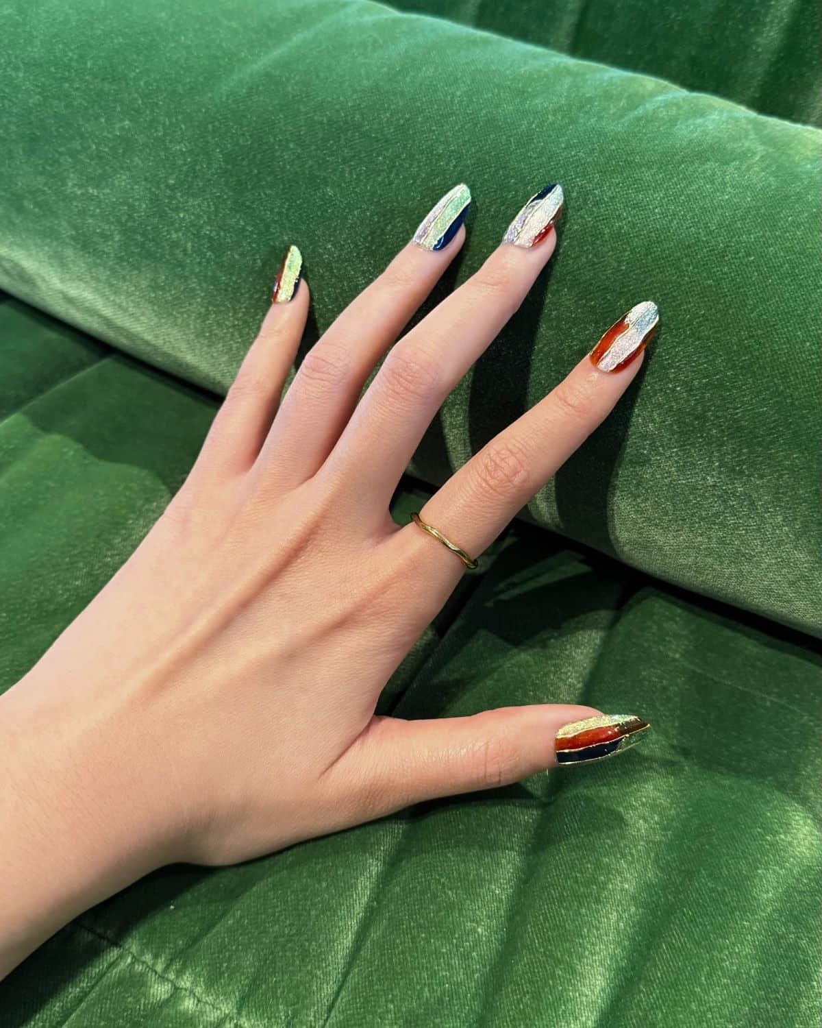 Press-on nails with minimal chic design against green couch fabric.