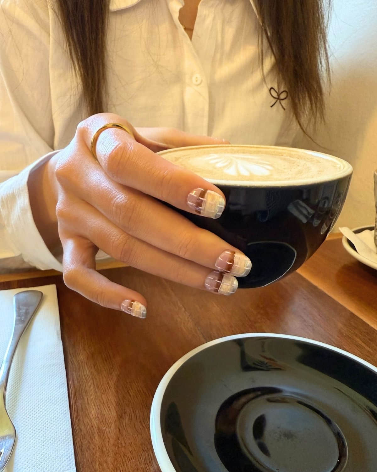 Reusable press-on nails holding latte in café with saucer.